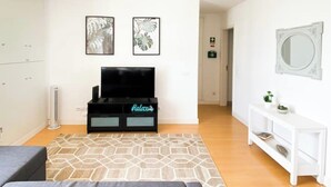 Un salon moderne doté d’un téléviseur à écran plat, d’un meuble de rangement noir, d’un tapis à motifs, d’une console blanche et d’un grand miroir mural.