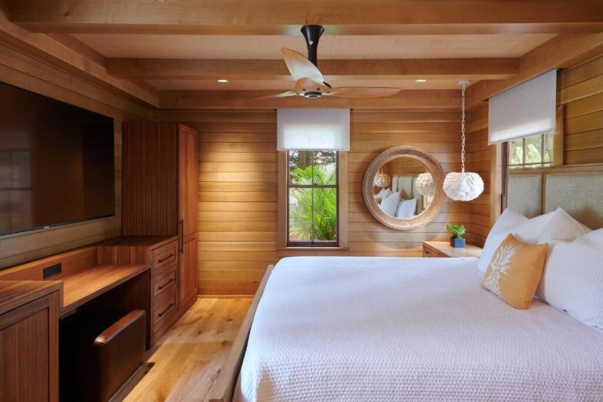 Una camera da letto con un letto grande, pareti in legno, una ventola a soffitto, una TV e una finestra vista verde.