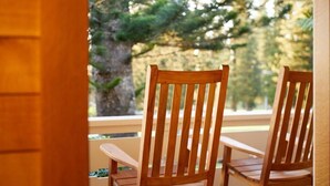 Two wooden chairs with vertical slats, positioned on a porch with a view of a tree and a building in the background. - Hotel Lanai (Lanai City)