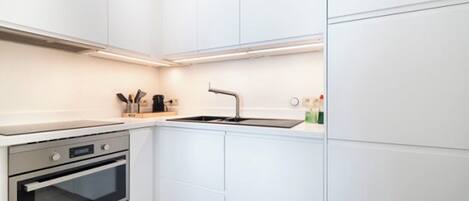 Una cocina moderna con armarios blancos, horno de acero inoxidable, fregadero y campana extractora.