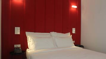 A hotel room with a red accent wall, a bed with white linens, a bedside table with a phone, and a nightstand with a lamp.