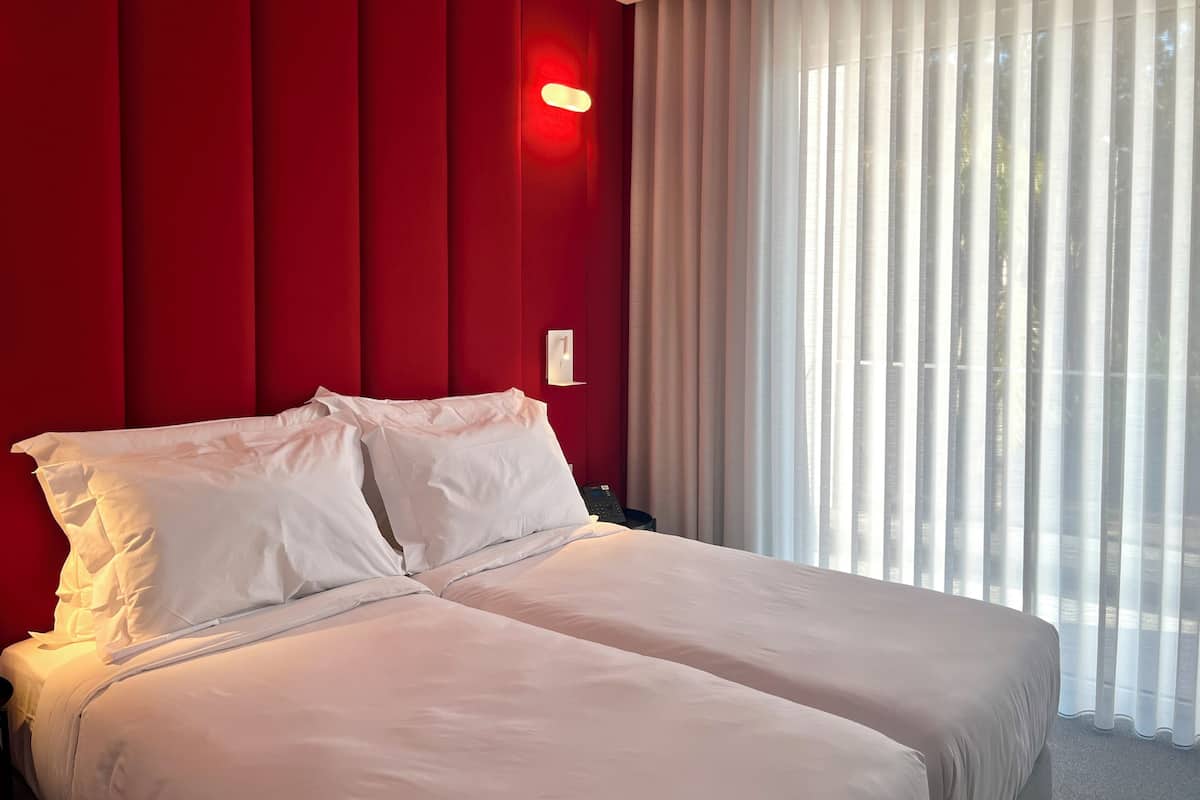 A hotel room with a large bed, red walls, and a window with sheer curtains.