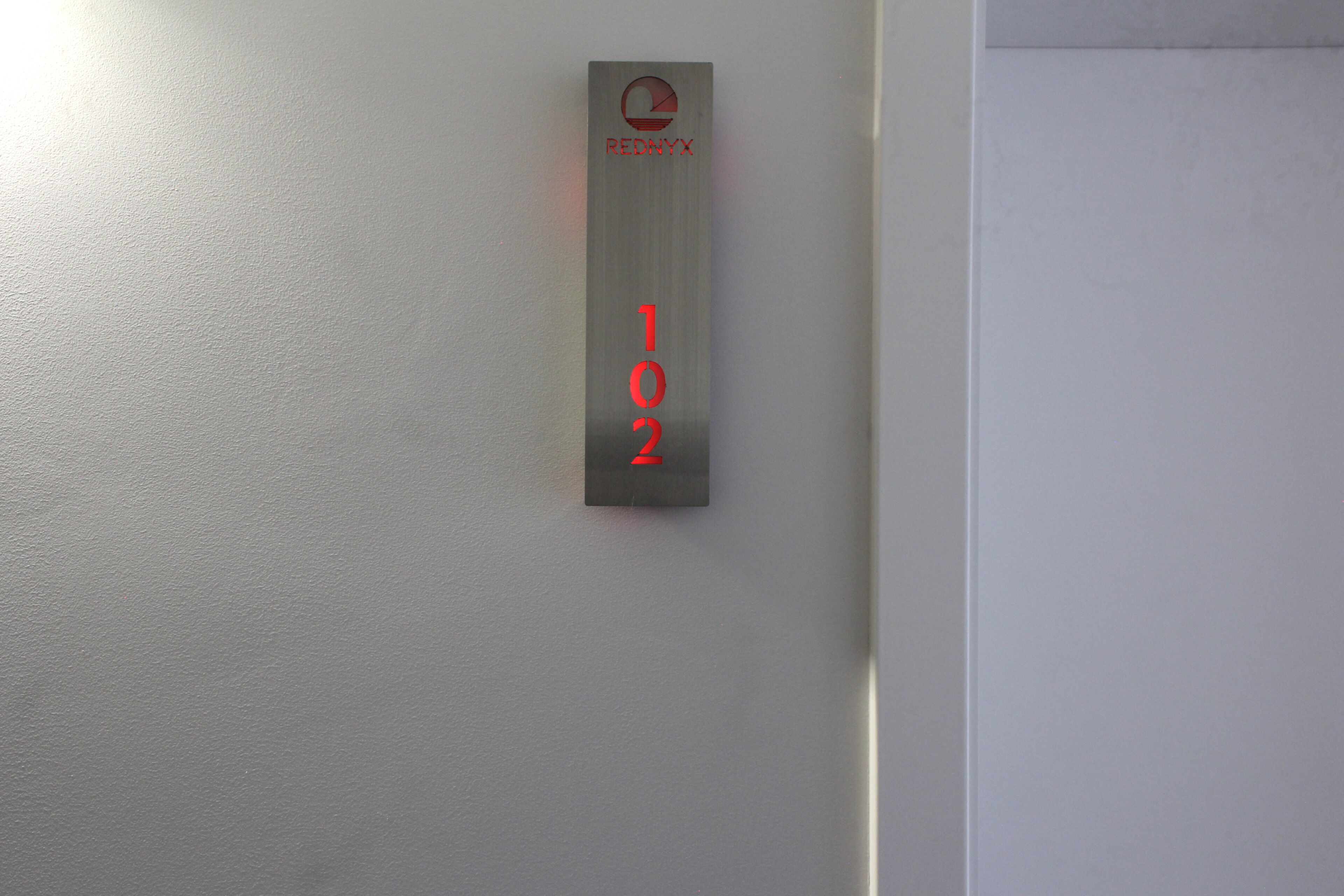 A metallic sign with the number 102 and a logo on a white wall.