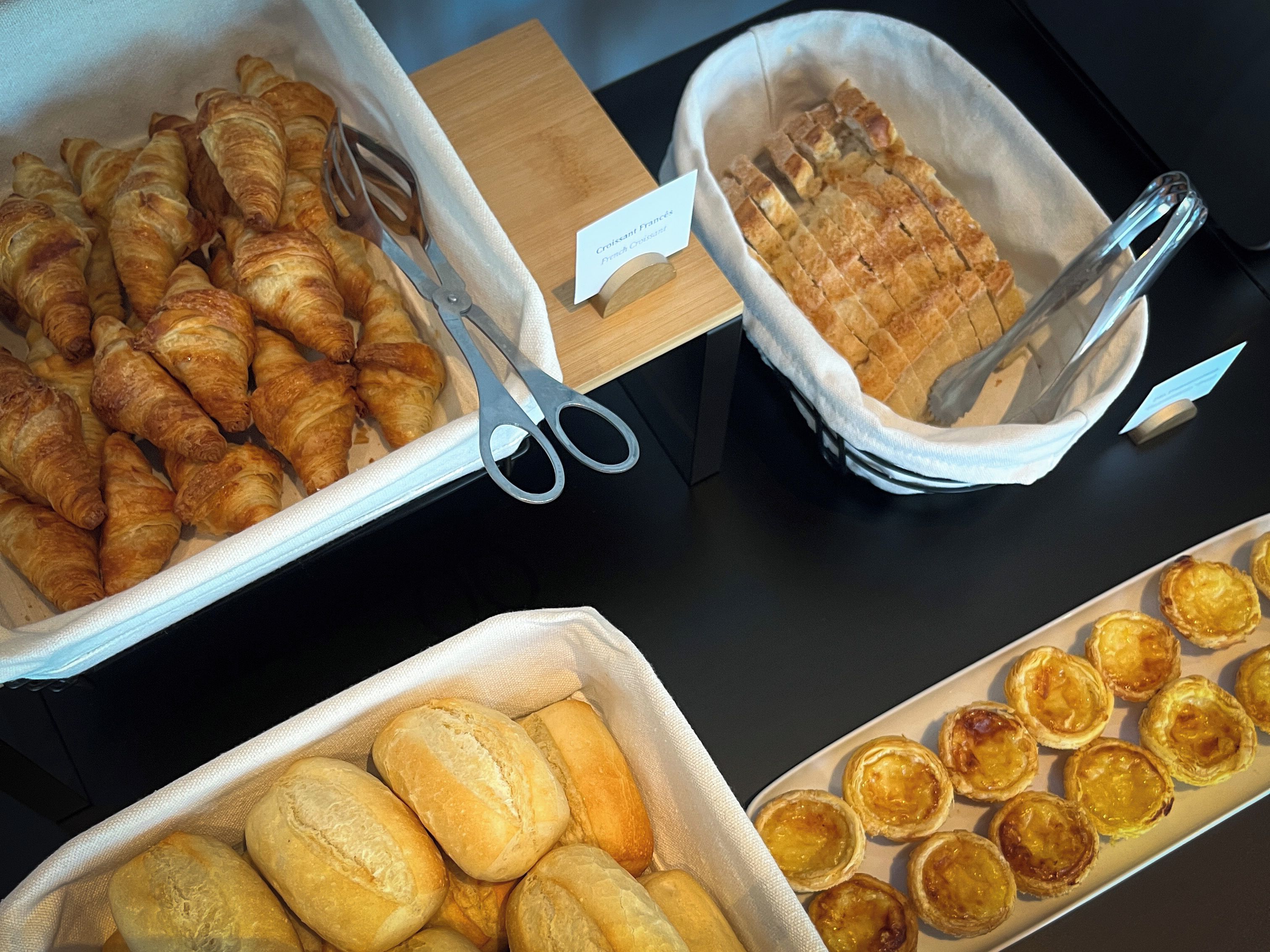 A buffet table with various baked goods including croissants, bread rolls, and pastries.