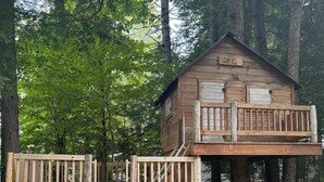 Eine Holzhütte mit Balkon und einer Holzterrasse, die durch eine Leiter erreichbar ist.