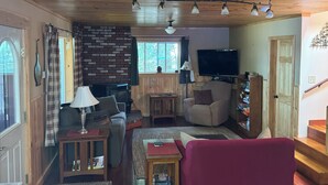 Ein gemütliches Wohnzimmer mit Holzboden, einem roten Sofa, einem Fernseher und einer Ziegelwand.