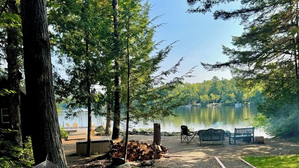 Ein Campingplatz mit einer Hängematte, Holzstoß, einer Bank und Blick auf einen See.