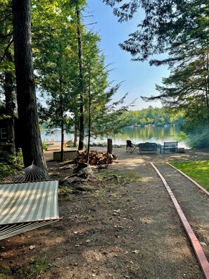 A campsite with a hammock, a pile of firewood, a bench, and a view of a lake. - Year-Round Lakefront Retreat with Cedar Barrel Sauna and Treehouse (Lincoln)