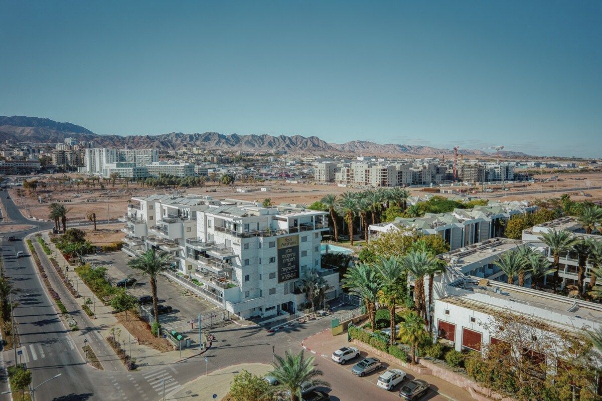 A multi-story building with a flat roof, surrounded by palm trees and a clear sky.