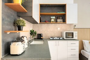 A compact kitchen with a toaster, kettle, microwave, and a small cabinet.