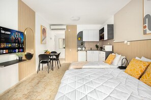 A modern hotel room with a bed, a desk, a chair, a TV, and a kitchenette.