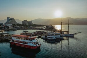 A harbor with boats, a large building, and mountains in the background.