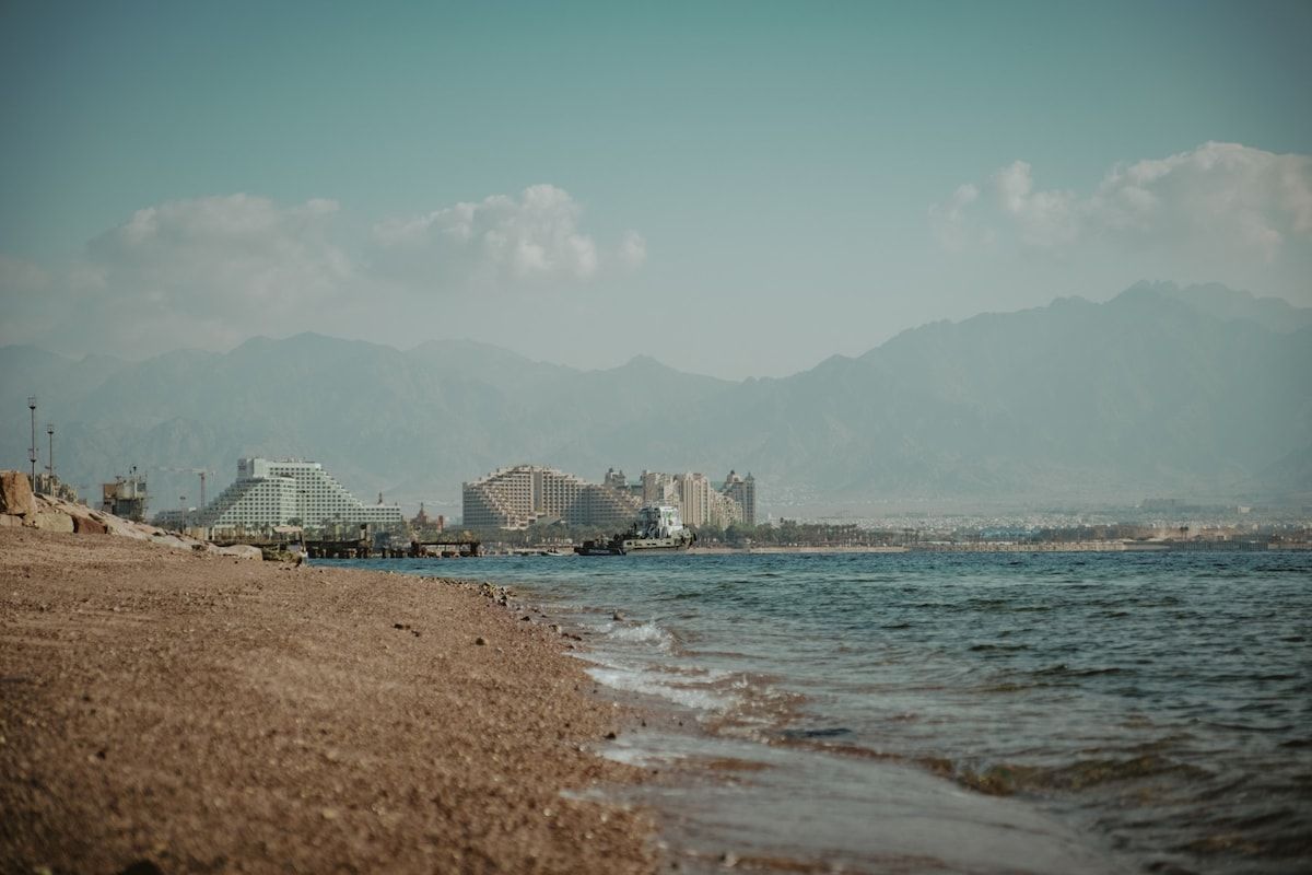 Ein Strand mit Gebäuden im Hintergrund, einem klaren Himmel und Bergen in der Ferne.