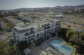 Un hotel de varios pisos con piscina en la azotea, rodeado de jardines y palmeras.