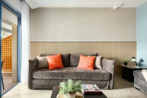 Un salón moderno con un sofá gris, dos almohadas naranjas, una mesita auxiliar con una lámpara y una planta en maceta sobre la mesa de centro.
