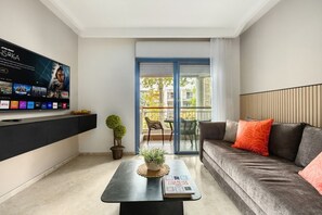 Una sala de estar moderna con un televisor de pantalla plana, un sofá, una mesa de centro y un balcón con vistas.