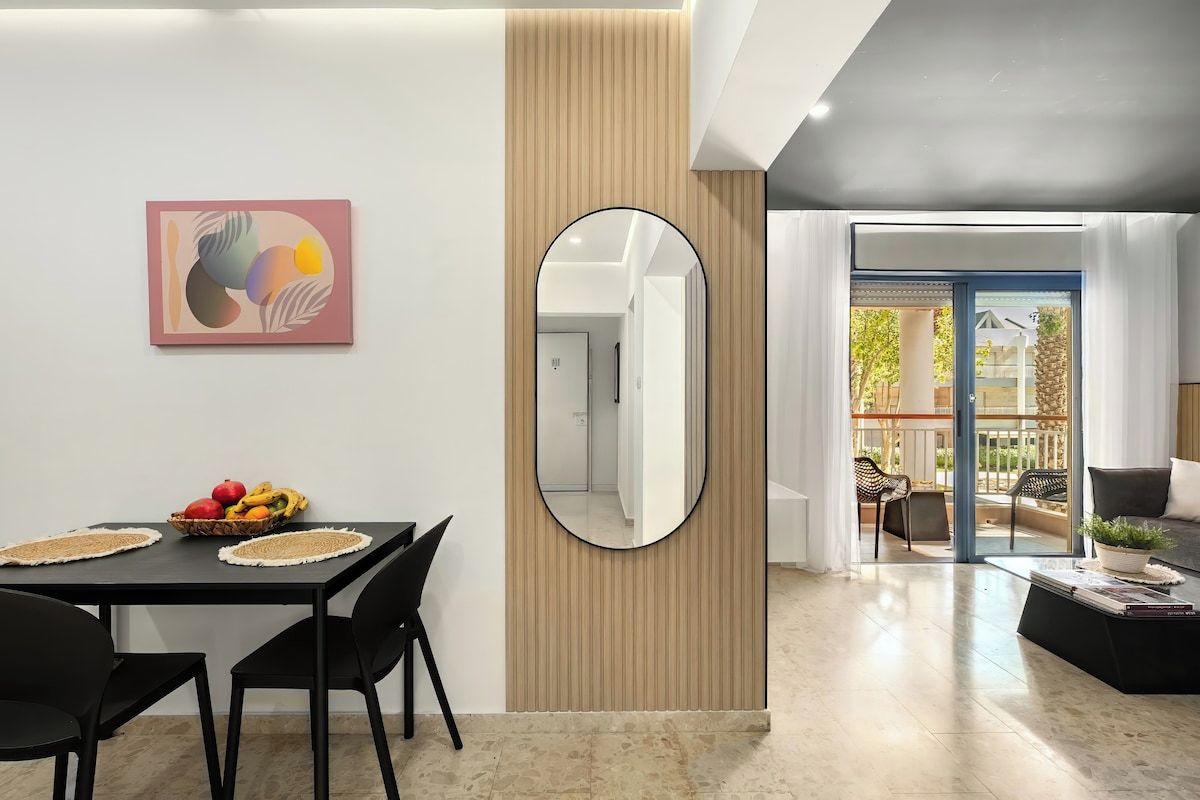 A modern living room with a dining area, a large mirror, and a view to the outside.
