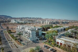 A multi-story building with a flat roof, surrounded by palm trees and a clear sky. - 1BR Royal Park Apt • Garden View by SeaNRent (Eilat)