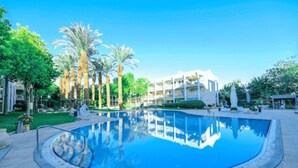 A swimming pool with a clear blue water surface, surrounded by a paved deck and palm trees. - Bright 1BR Royal Park Apt with Garden View (Eilat)