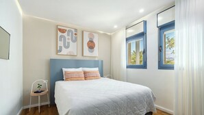 A bedroom with a bed, a chair, and two windows with curtains. - Bright 1BR Royal Park Apt with Garden View (Eilat)