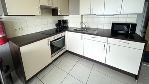A compact kitchen with white cabinets, a black countertop, a built-in oven, a microwave, and a coffee maker. - Studio in Middelkerke With Pool and Sea View (Middelkerke)