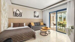Habitación de hotel moderna con cama, sofá y una pequeña mesa. Incluye obras de arte abstractas en las paredes y vistas al exterior.