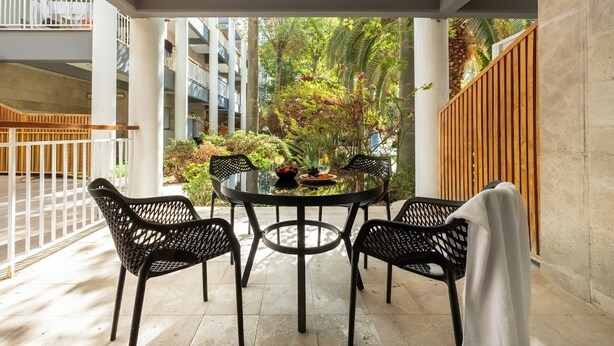 Un espacio al aire libre cubierto con una mesa redonda y cuatro sillas, rodeado de follaje y vistas a edificios.