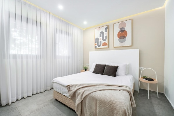 A modern bedroom with a large bed, white curtains, and two wall-mounted artworks.
