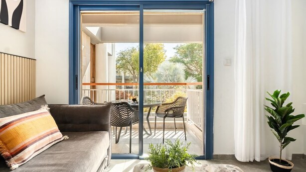Una stanza con un divano, un tavolo da pranzo con sedie, una pianta in vaso e una porta scorrevole in vetro che dà su un balcone esterno.