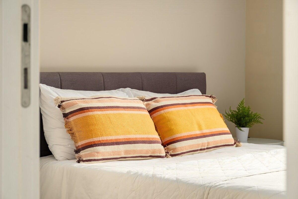 A bed with two striped pillows, a grey headboard, and a small potted plant on the side.