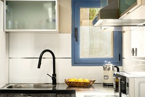 A kitchen with a stainless steel sink, a black faucet, a window with a blue frame, and a basket of lemons on the counter. - Serene Royal Park Stay | Comfort & Ease (Eilat)