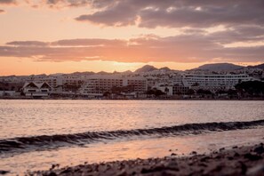 A coastal cityscape with buildings along the waterfront, a clear sky, and a sunset.