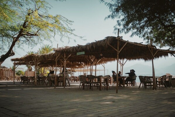 An outdoor seating area with thatched umbrellas, wooden tables, and chairs.