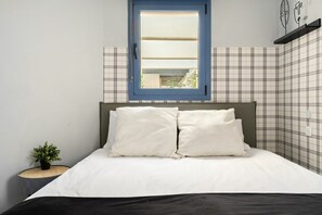 A bedroom with a bed, a window, a nightstand with a plant, and a wall with a checkered pattern.