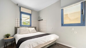 Une chambre à coucher avec un lit, une table de chevet ornée d’une plante, une fenêtre et une étagère fixée au mur.
