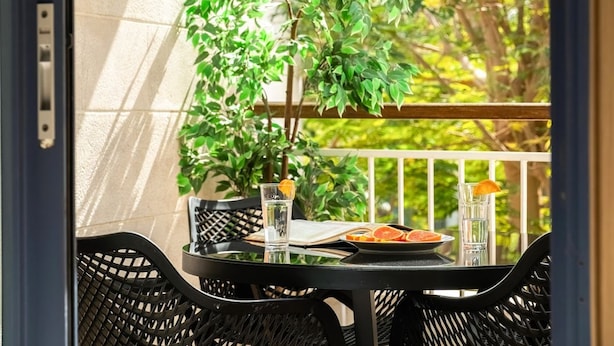 Un balcon avec une table, des chaises, un pot de fleurs et un plateau sur lequel se trouvent une assiette et des verres.