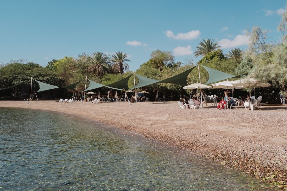 Ein Strand mit klarem Wasser, Sonnenschirmen und Menschen.