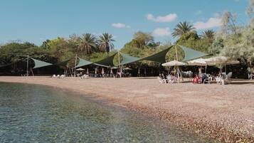 Ein Strand mit klarem Wasser, Sonnenschirmen und Menschen.