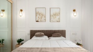 A bedroom with a large bed, two wall-mounted light fixtures, and two framed artworks on the wall.