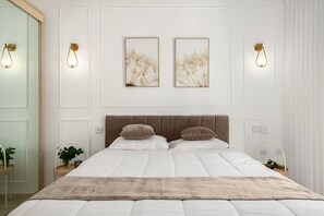 Un dormitorio con una cama grande, dos lámparas fijadas a la pared y dos cuadros enmarcados.
