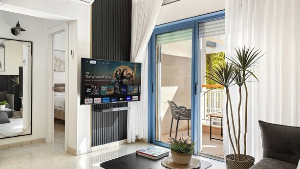 A modern living room with a flat-screen TV, a coffee table with a book, a potted plant, and a sofa. - Bright 2BR Apartment with Balcony at Royal Park (Eilat)