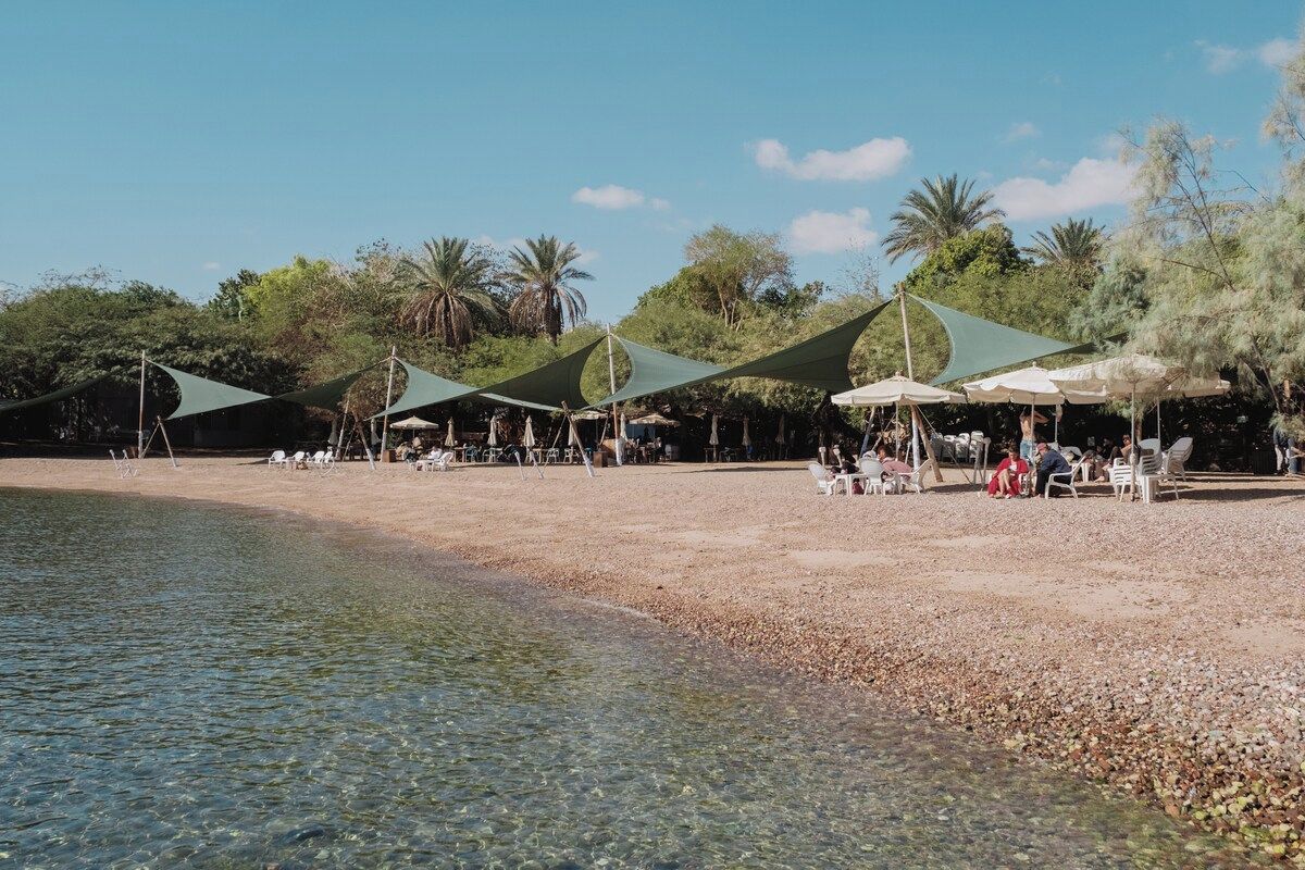 Una playa con agua cristalina, sombrillas y gente.