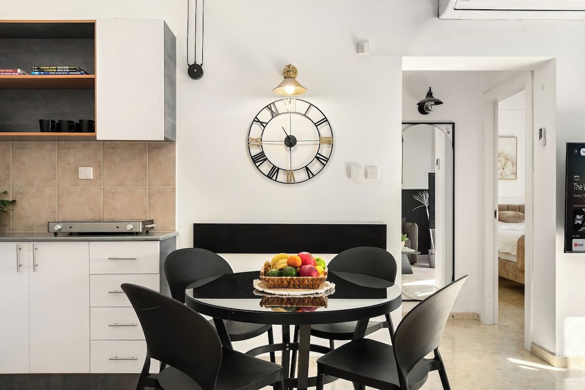 Una cocina moderna con armarios blancos, una mesa redonda con sillas negras y un reloj de pared.