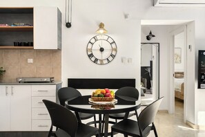 Una cucina moderna con mobili bianchi, un tavolo rotondo con sedie nere e un orologio a parete.