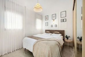 A bedroom with a bed, a bedside table, a hanging light fixture, and framed pictures on the wall. - 2BR Apt • Balcony • Royal Park by SeaNRent (Eilat)