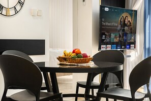 Un comedor moderno con una mesa redonda, sillas negras y una cesta de frutas.