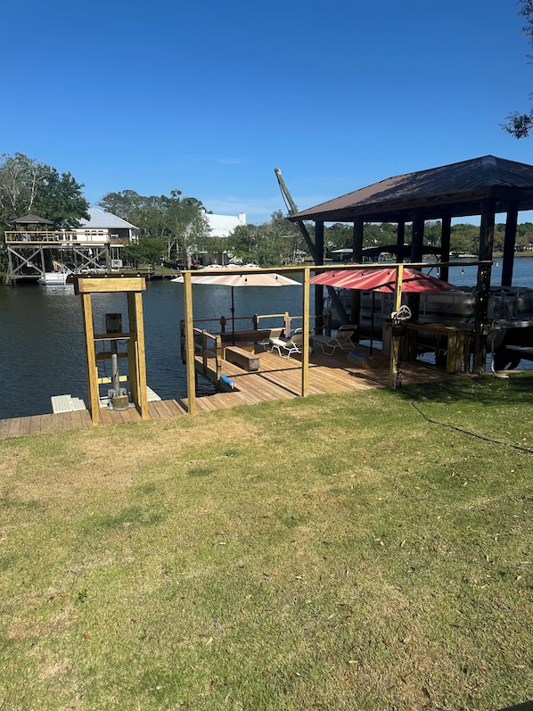 A dock with a covered seating area, a boat, and a building in the background.
