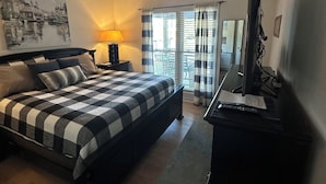 Un dormitorio con cama, escritorio, ventilador de techo, ventana con cortinas y un cuadro en la pared.