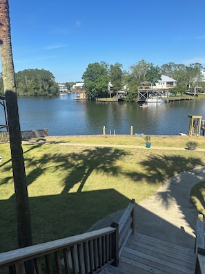 A lakeside view with a wooden deck, a boat dock, and houses across the water.