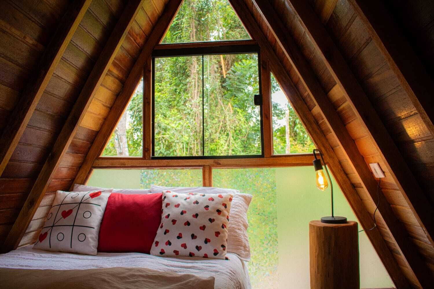 A bedroom with a sloped ceiling, a large window, and a bedside lamp.